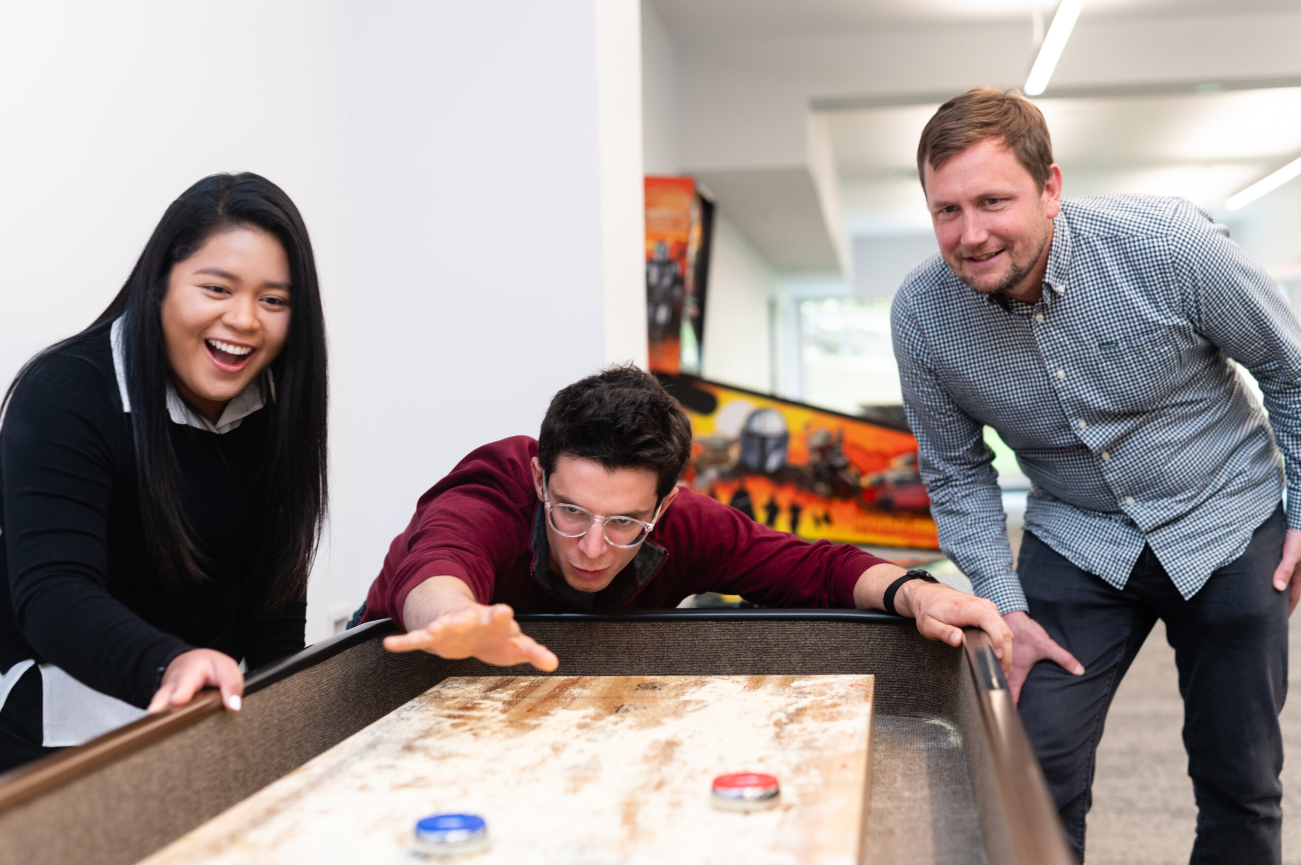 Three colleagues playing shuffleboard during a break in an office game room.