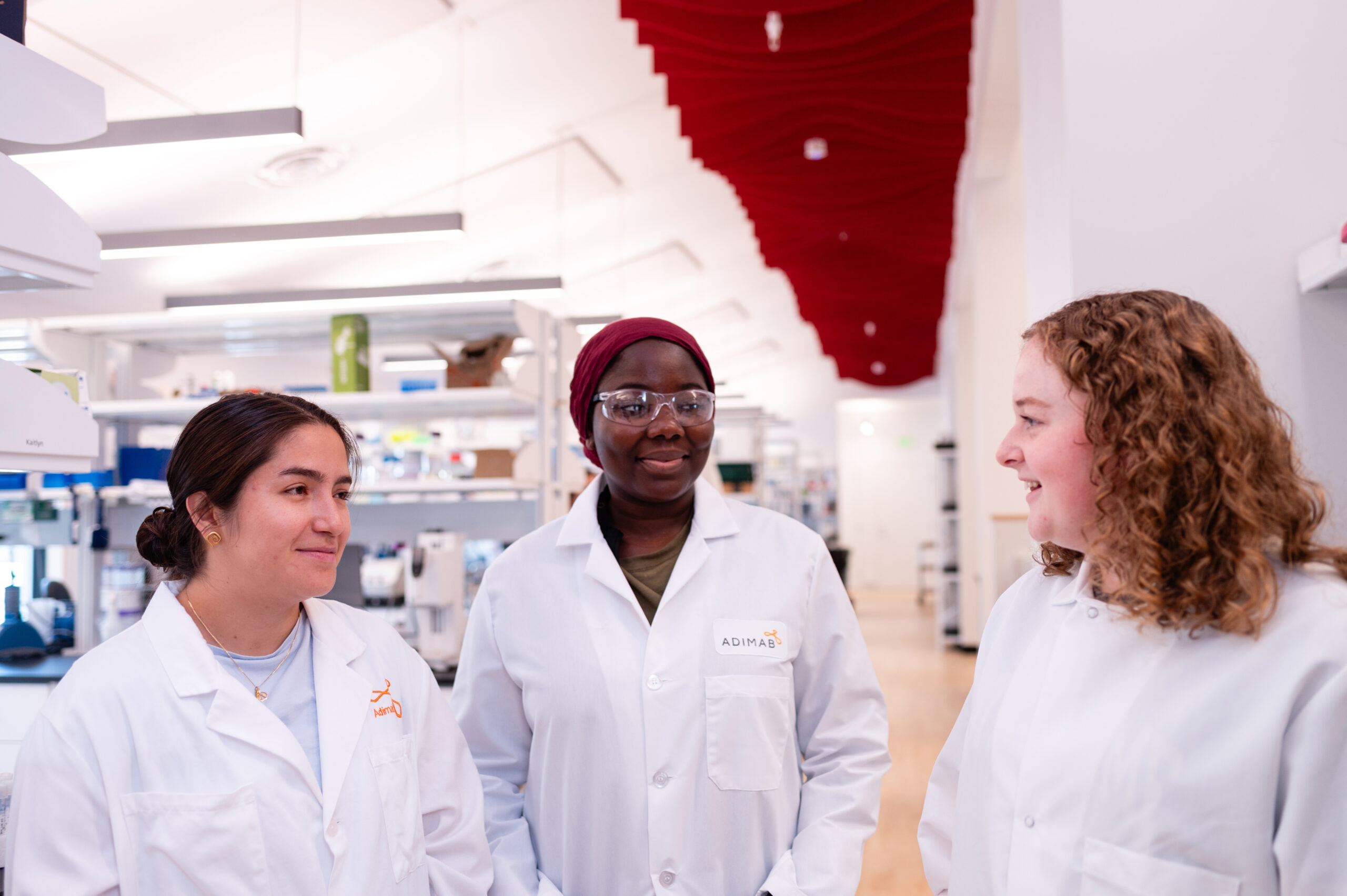 Three scientists in lab coats having a conversation in a bright, modern laboratory.
