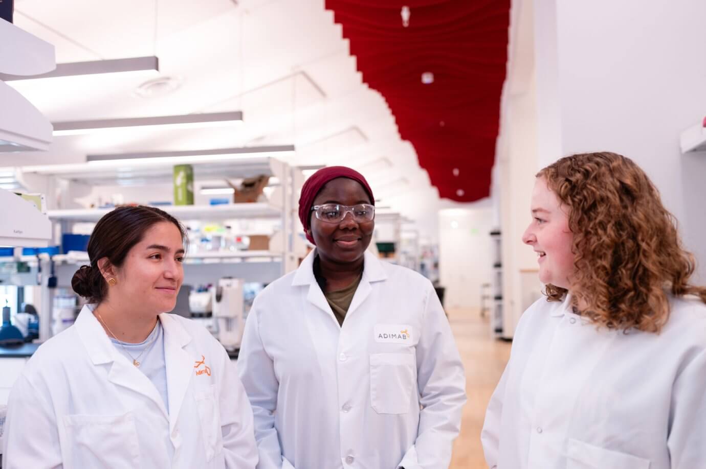 Three scientists in lab coats having a conversation in a bright, modern laboratory.