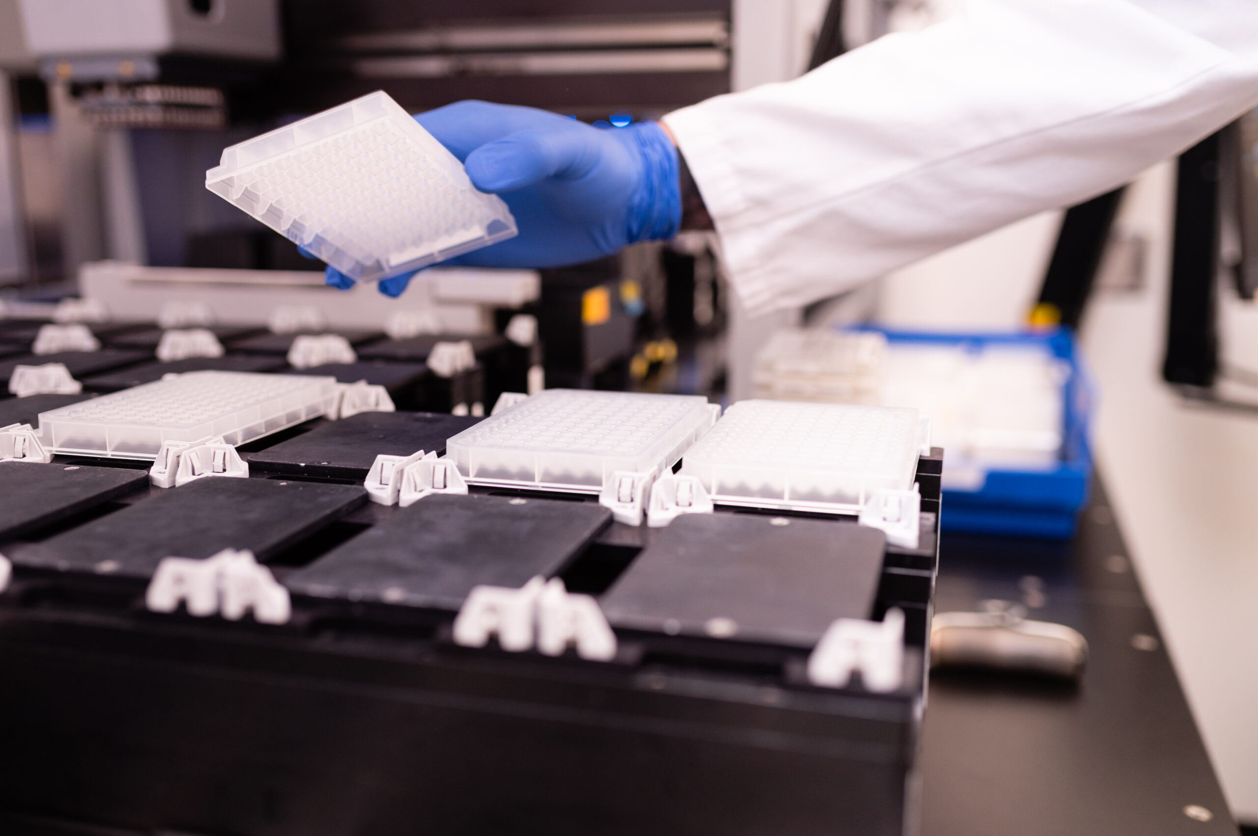 Gloved scientist loading 96-well plates into automated lab equipment.