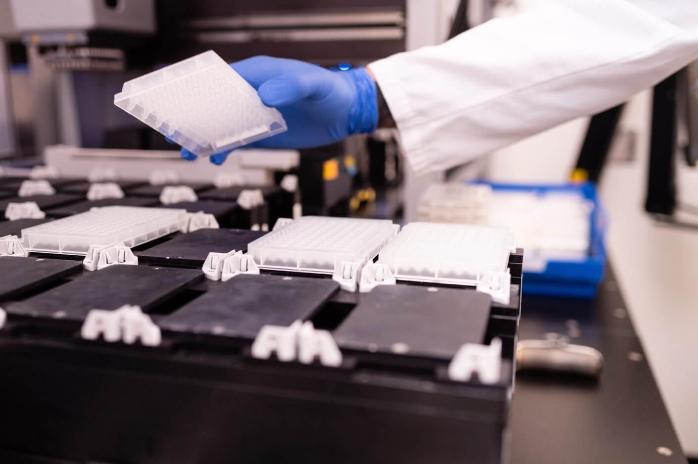 Gloved scientist loading 96-well plates into automated lab equipment.