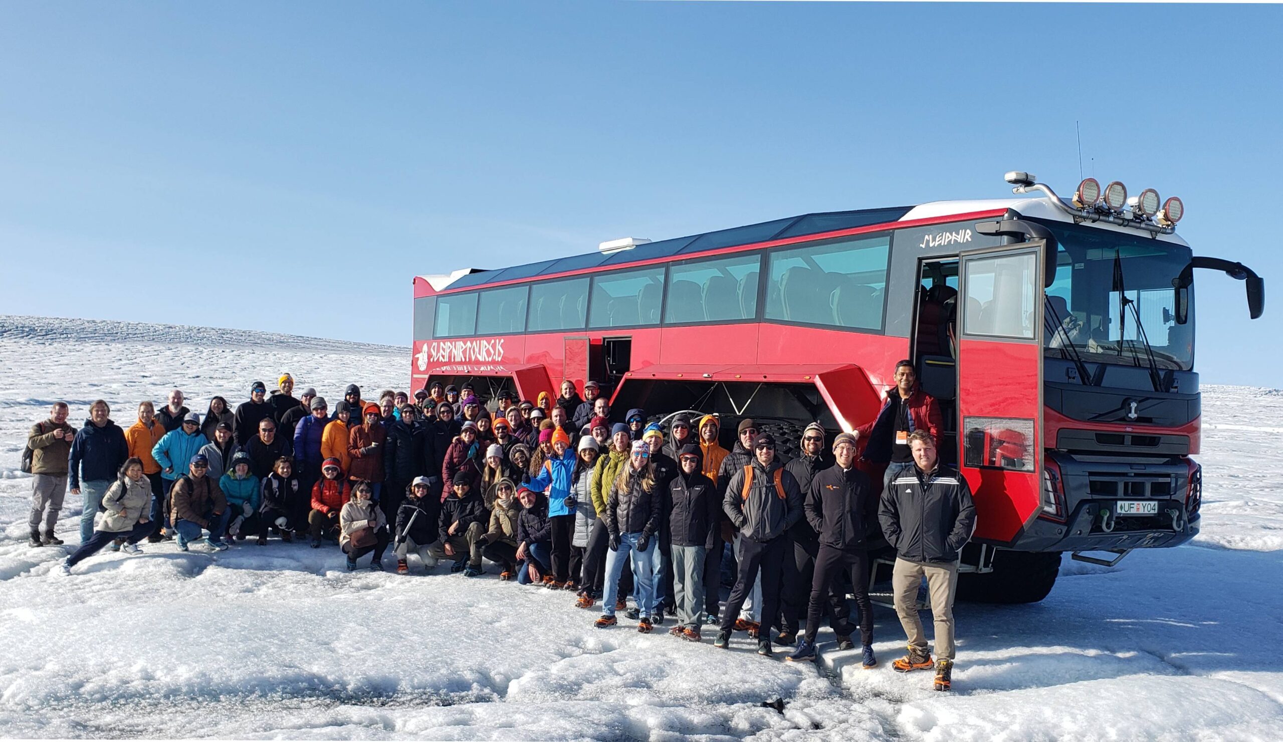 A group of people posing in front of a tour bus on a snowy landscape.