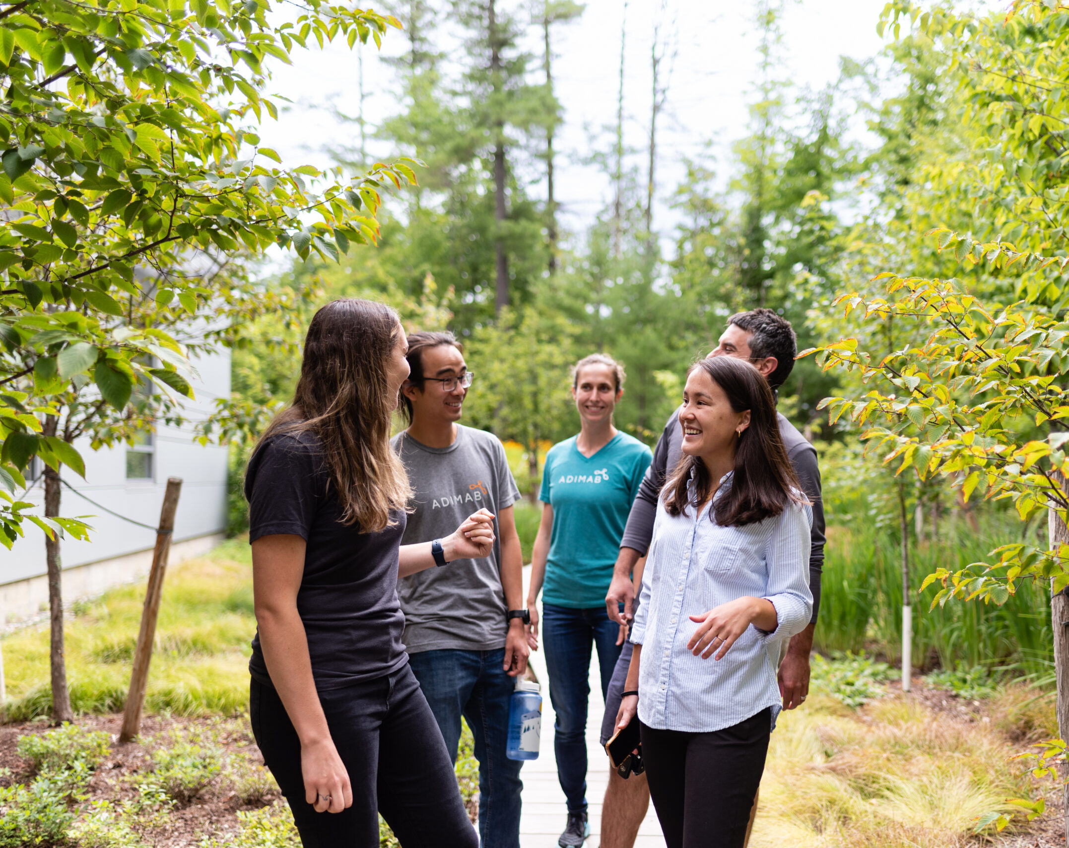 Group of Adimab team members walking and talking outdoors on a wooded path.