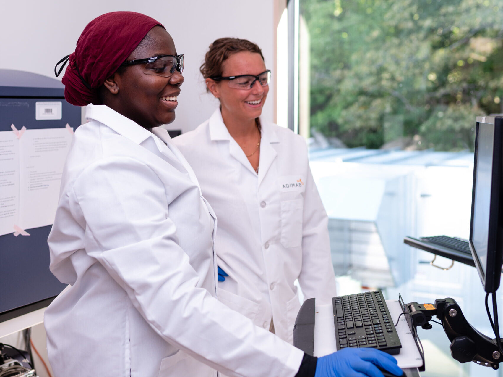 Two scientists in lab coats reviewing data on a computer in the laboratory setting.