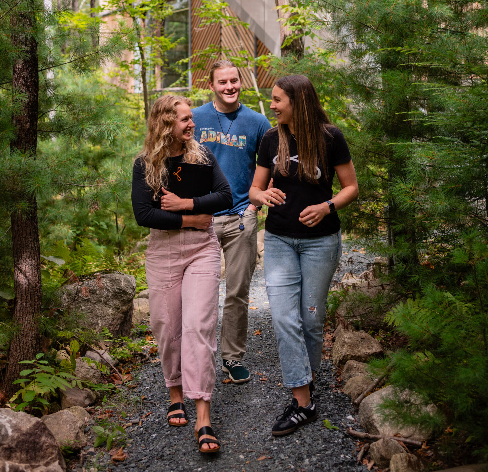 Three Adimab team members walking and talking on a wooded path outside the office.